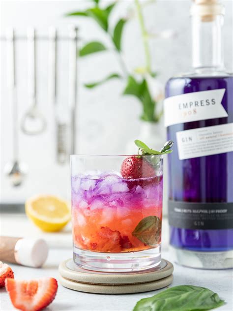 a glass filled with ice and strawberries next to a bottle of blueberry gin