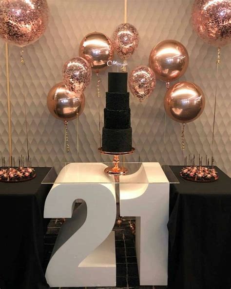 a black and white table topped with lots of gold balloons next to a number two cake