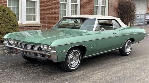 an old green car parked in front of a brick building