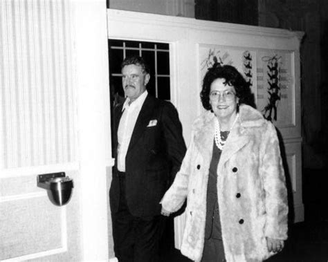 an old black and white photo of two people standing in front of a door, one wearing a fur coat