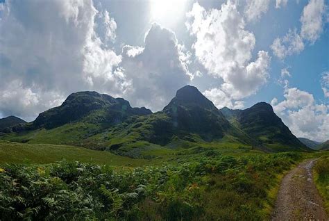 the sun shines brightly in the mountains above a dirt road and lush green hills