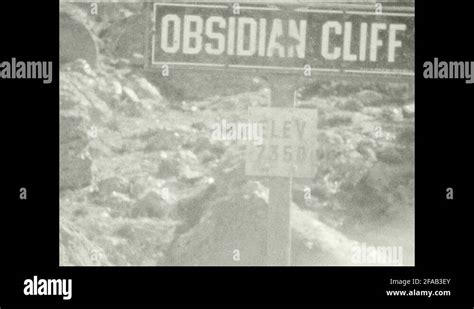 1920s: Sign for Obsidian Cliff and view of cliff. Parking lot in front ...