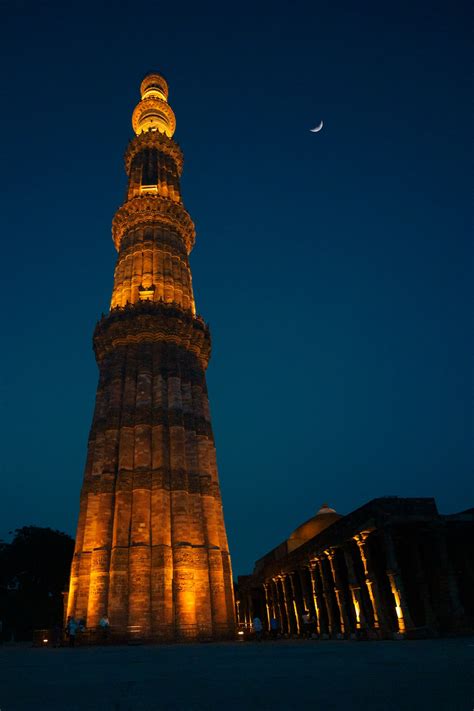 A tall tower with lights at night with Qutub Minar in the background ...