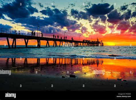 People stroll on Glenelg jetty at sunset sky splashed with colourful ...