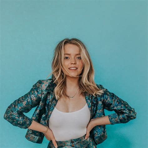 a woman standing in front of a blue wall with her hands on her hips and arms behind her back