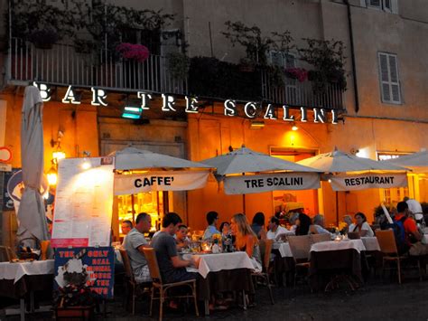 people are sitting at tables in front of a restaurant with umbrellas over them and lights on