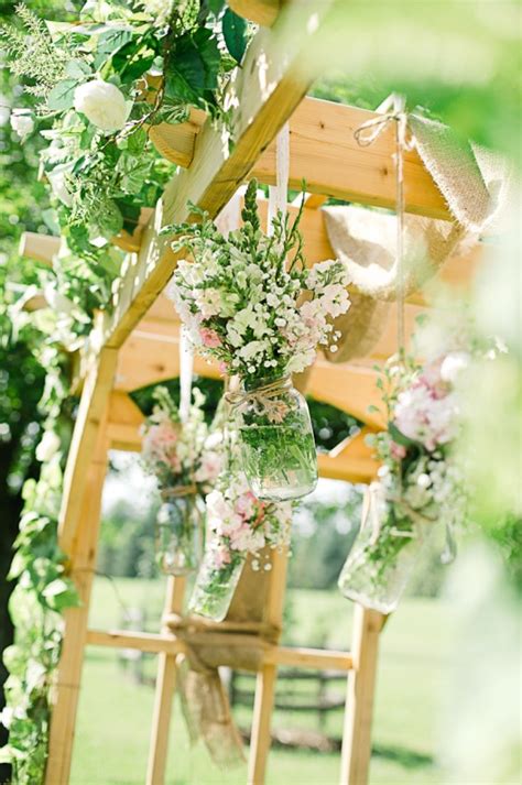 an outdoor ceremony with flowers and greenery in mason jars hanging ...