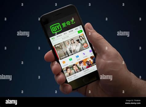 A man looks at his iPhone which displays the Iqiyi logo (Editorial use only Stock Photo - Alamy