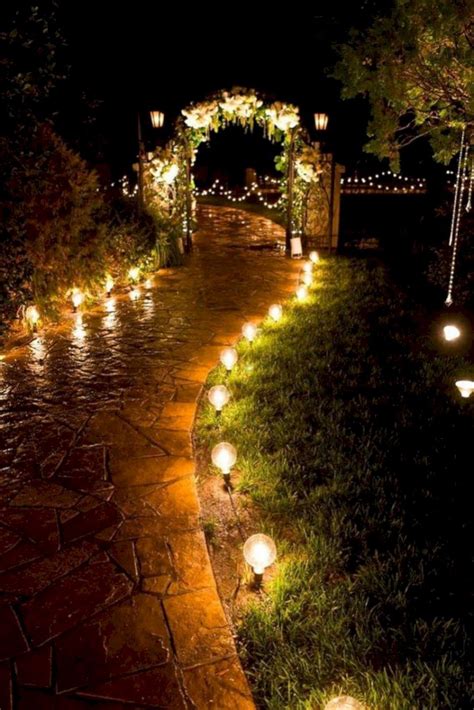 some lights are lit up in the dark on a path that is surrounded by grass