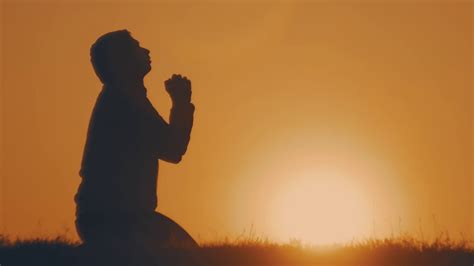 Silhouette young man praying outside at beautiful sunset. Male asks for ...