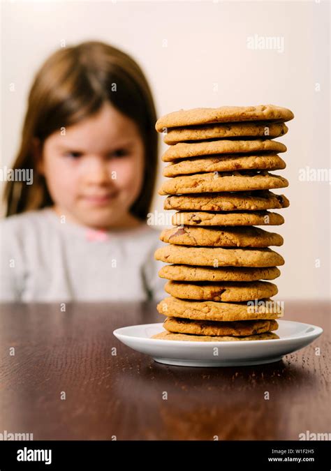Photo of a young girl staring at a tall pile of chocolate chip cookies. Focus on the cookies ...