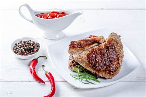 Two hot beef steaks on a white table with chili pepper and sauce - Creative Commons Bilder