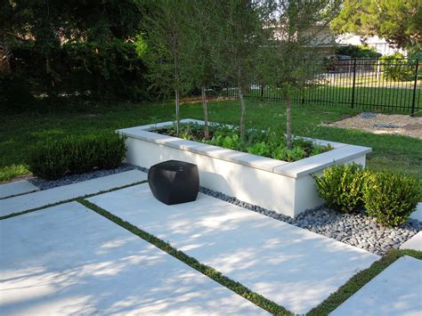 an outdoor garden area with white concrete and green plants in the center, surrounded by black ...
