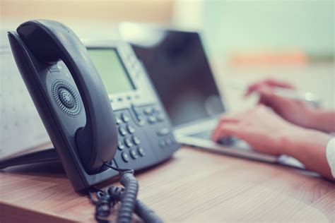 close up handset telephone VOIP with employee man working on laptop computer at office desk for ...