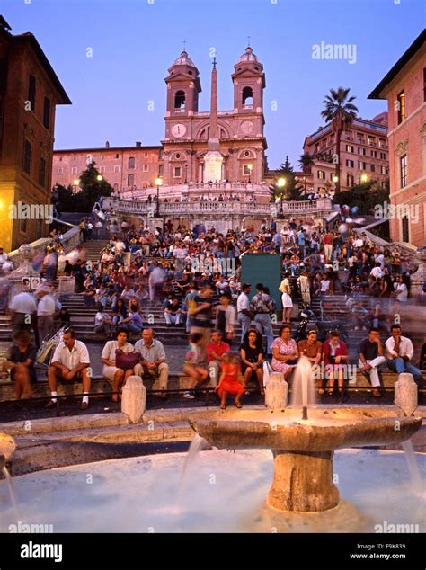 Tourists sitting on the Spanish Steps with a fountain in the foreground ...