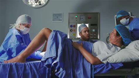 Side view of Caucasian female surgeon examining pregnant woman during labor in operation theater ...