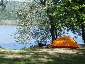 a tent pitched up next to the water with trees around it and camping gear on the ground