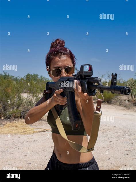 A Caucasian Latina woman posing with a Russian AK-47 assault rifle with American holo sight in ...