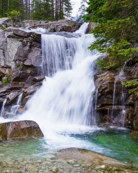 A gorgeous mountain waterfall flows among green forest and runs down the beautiful gray stones ...