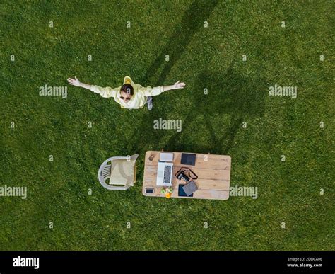 Aerial view of woman standing with raised arms in front of coffee table set on green lawn Stock ...