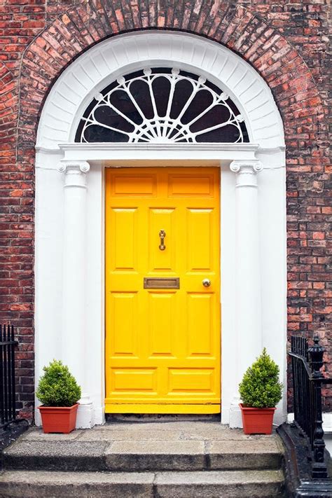 a yellow door with two potted plants on the steps in front of an old ...