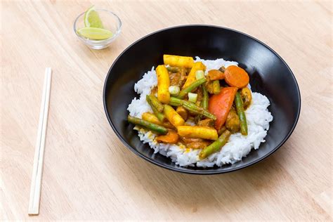 Top View Food Photo of Vegetarian Thai Curry with Rice in Black Ceramic Bowl next to Chopsticks ...