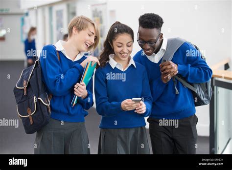 Three smiling students wearing blue school uniforms with mobile phone in school corridor Stock ...