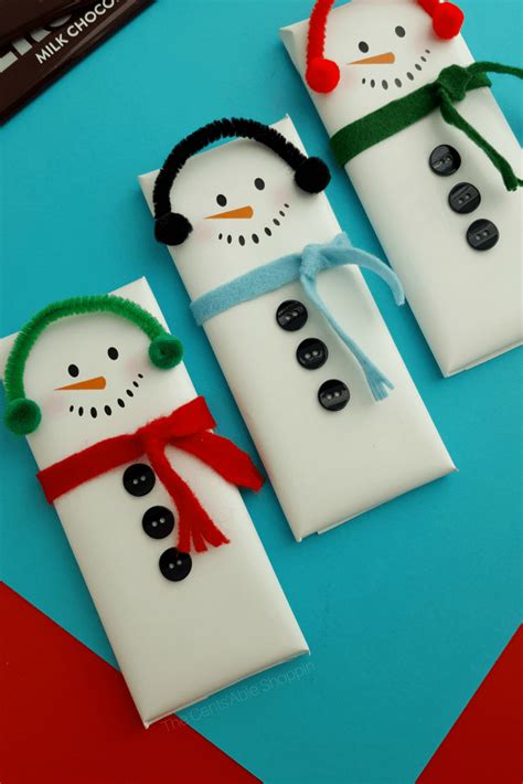 three snowmen made out of candy wrappers on a blue surface with red and green ribbon