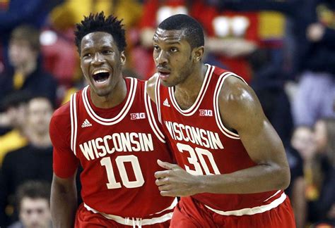 two men in red uniforms standing next to each other on a basketball court with fans watching