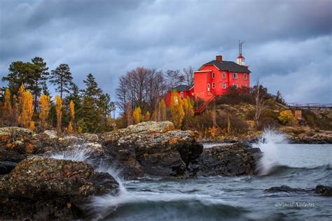 a red house sitting on top of a rocky cliff next to a body of water