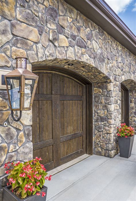 two planters with flowers in front of a stone wall and wooden doors on the side of a house