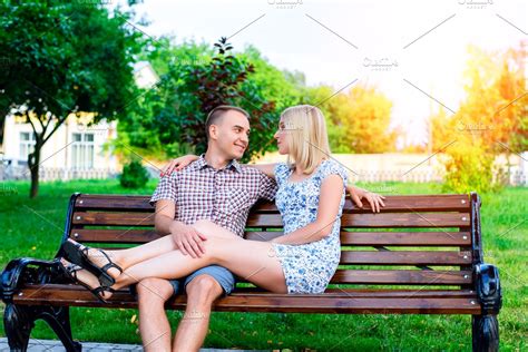 Young couple man and woman sitting on a bench hugging in park ribbon, declaration of love ...