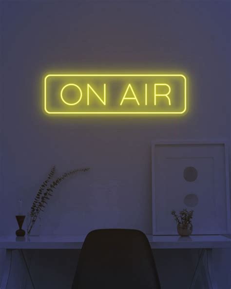 a neon sign that reads on air above a desk with a chair and plant in ...