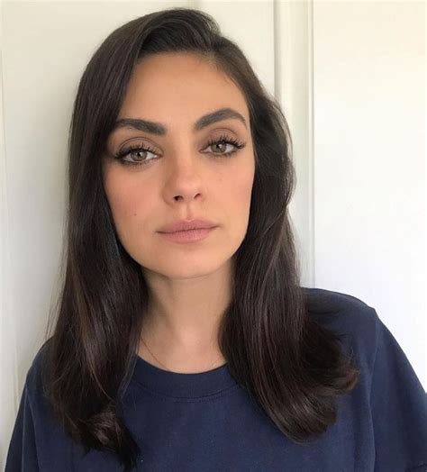 a woman with long dark hair wearing a blue shirt and looking at the camera while standing in ...