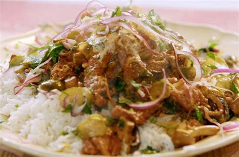 a white plate topped with rice and meat covered in sauce on top of a wooden table