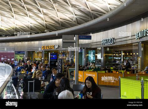 The main dining area of King's Cross station with restaurants and diners seated outside, London ...