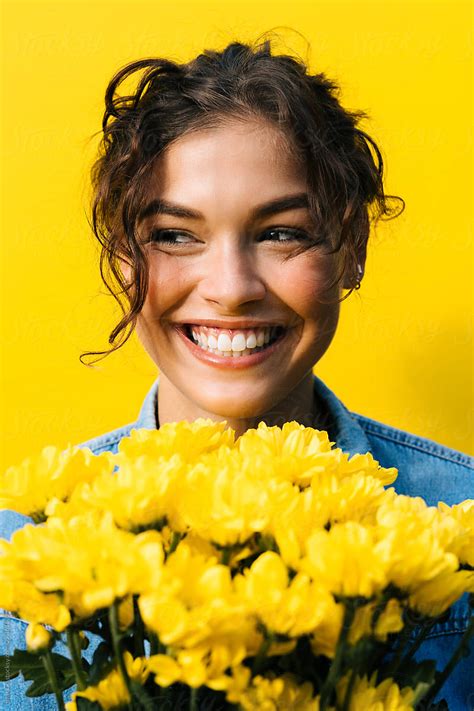 a smiling woman holding yellow flowers in front of her face by luma studio for stocks
