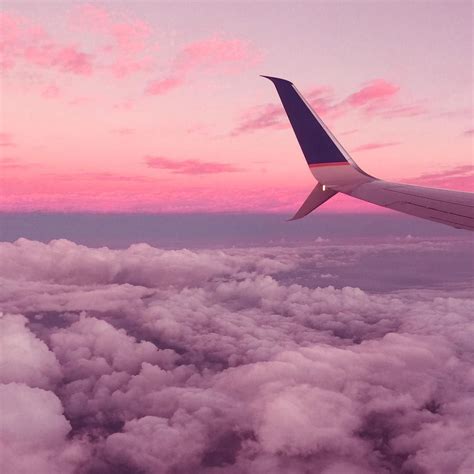 the wing of an airplane flying over clouds at sunset or dawn with pink ...