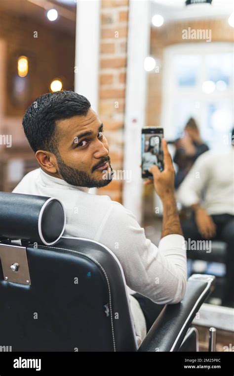 Young man taking mirror selfie after having his hair cut at barbershop ...