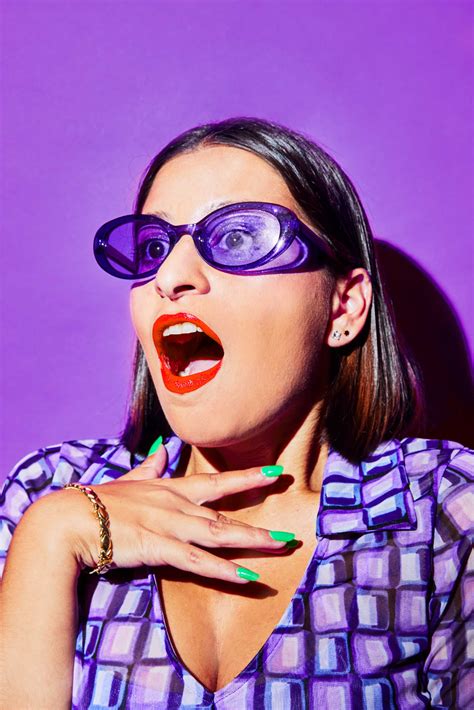 a woman with purple glasses on her face and green nail polish in front of a purple background