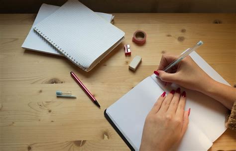 Top View Photo of Person writing in blank Notebook with Papers, Sharpener, Eraser and Tape on ...