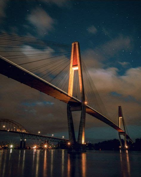 a large bridge over water at night with lights on it's sides and stars ...