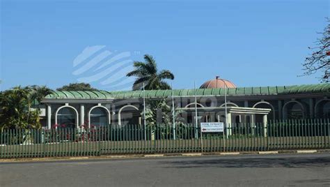 a large building with a green roof next to a fence and palm trees in ...