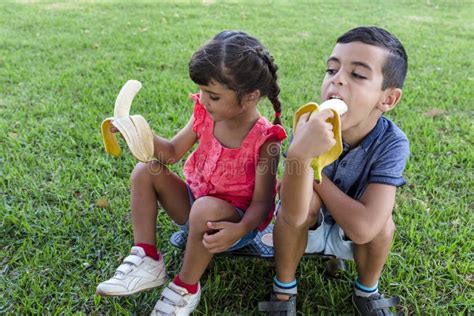 Two Kids Eating Banana Sitting Outdoors on the Grass in a Park. Stock ...