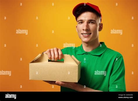 Delivery person holding parcel with food delivery against yellow background Stock Photo - Alamy