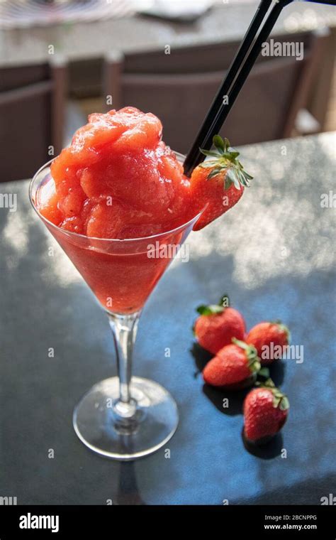 a tasty frozen strawberry daiquiri cocktail alongside some fresh strawberries Stock Photo - Alamy