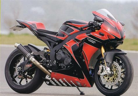 a red and black motorcycle parked on the side of a road with grass in ...