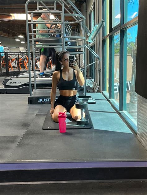 a woman is sitting on the floor in front of a gym machine and holding a pink cup