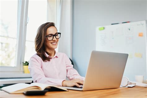 Smiling young woman working in office with laptop - Smartsys