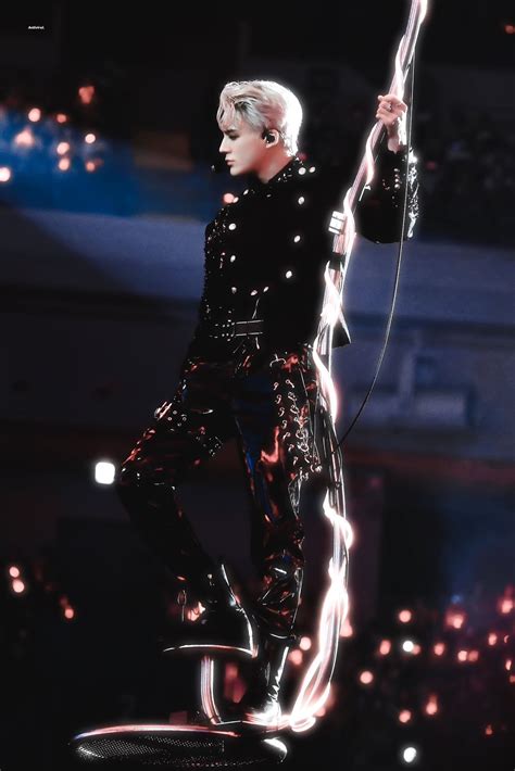 a male in a black outfit is performing on a stage with some lights behind him